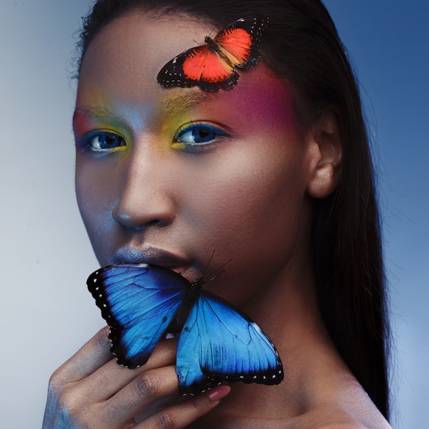 Joven y bella modelo negro de aspecto exótico con mariposa azul brillante