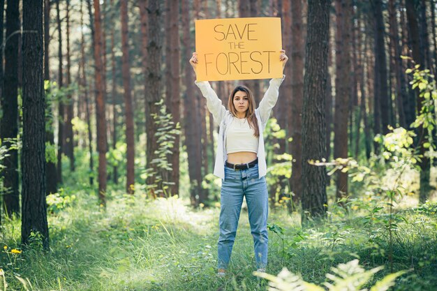 Joven y bella mujer activista voluntaria en el bosque con un cartel salva el bosque