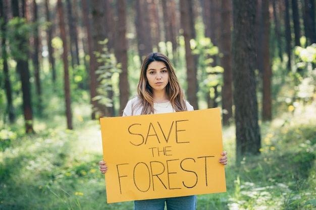 Joven y bella mujer activista voluntaria en el bosque con un cartel salva el bosque