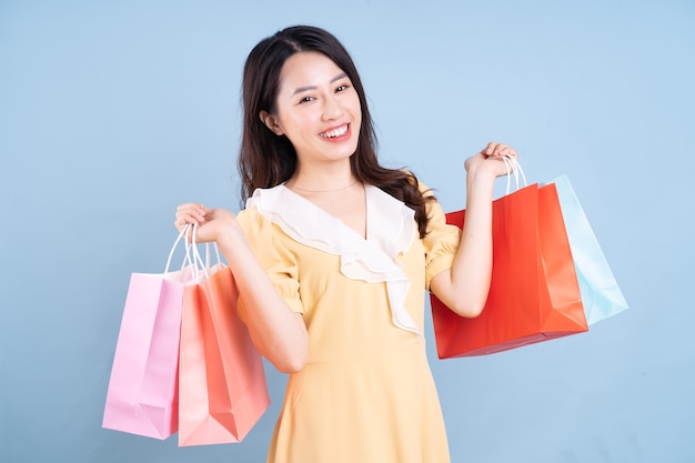 Joven y bella mujer asiática con bolsa de compras sobre fondo azul.