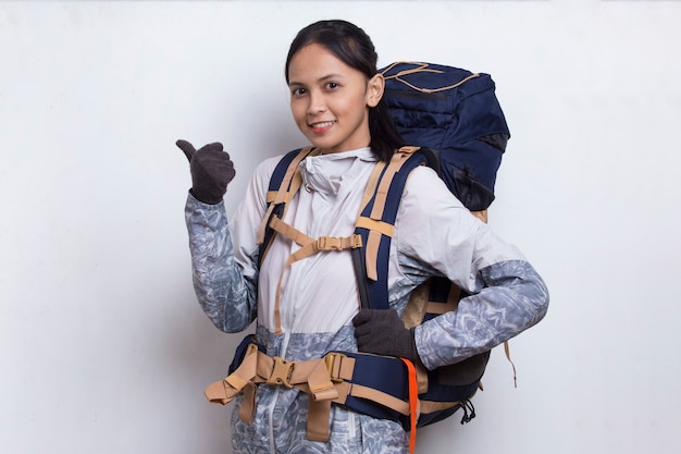 Joven y bella mujer asiática excursionista con mochila mostrando un pulgar hacia arriba gesto ok sobre fondo blanco.