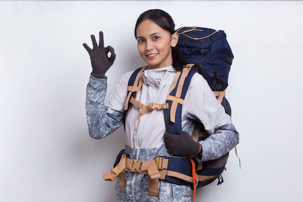 Joven y bella mujer asiática excursionista con mochila mostrando un pulgar hacia arriba gesto ok sobre fondo blanco.