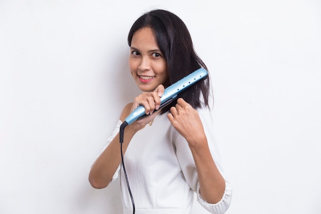 Joven y bella mujer asiática feliz alisar el cabello con plancha de pelo en blanco