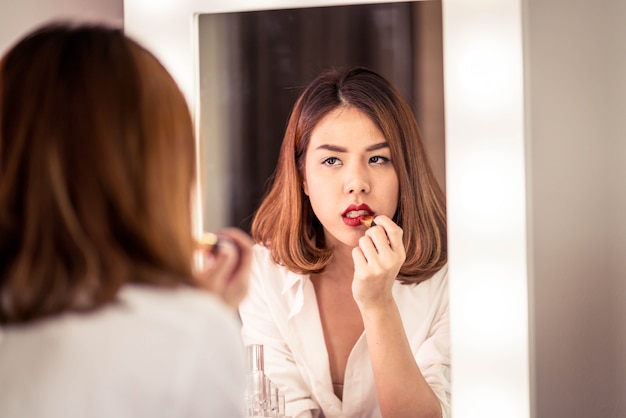 Joven y bella mujer asiática haciendo maquillaje cerca de espejo