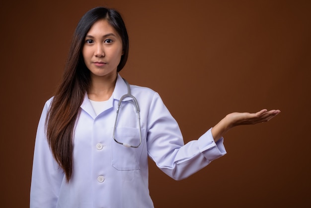 Joven y bella mujer asiática médico sobre fondo marrón