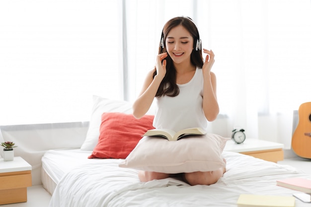 Joven y bella mujer asiática relajante escuchando música con auriculares en la cama en su casa