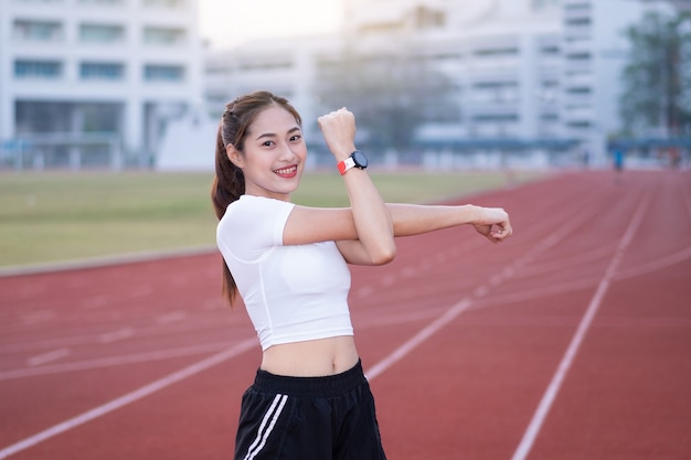 Una joven y bella mujer asiática en ropa deportiva haciendo estiramientos antes de hacer ejercicio al aire libre en el parque por la mañana para conseguir un estilo de vida saludable. Mujer joven sana calentando al aire libre