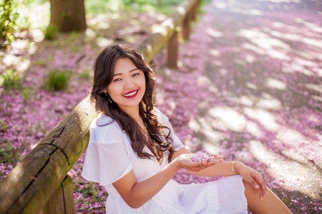 Una joven y bella mujer asiática con un vestido blanco camina en un parque de flores. Sakura. Árboles florecientes. Primavera.