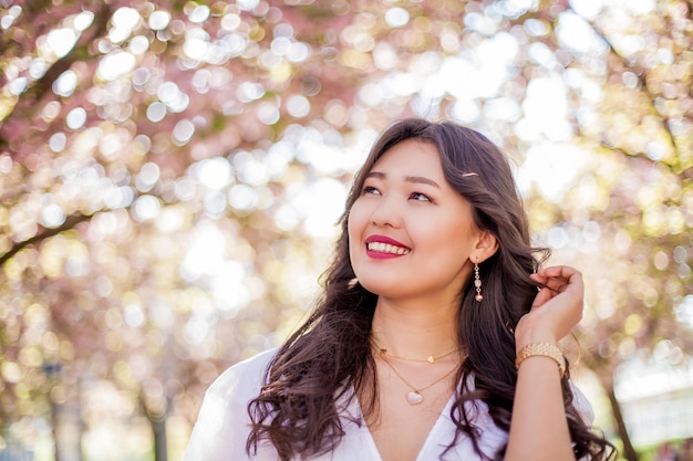 Una joven y bella mujer asiática con un vestido blanco camina en un parque de flores