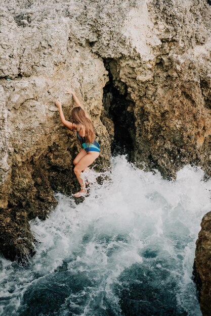 Una joven y bella mujer bronceada con el pelo largo en bikini azul sentado en las rocas cerca de azul verde claro