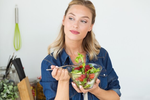 Joven y bella mujer comiendo ensalada en casa.