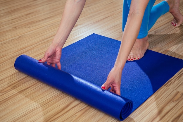 Una joven y bella mujer despliega una estera de entrenamiento para yoga en un piso de madera. alfombra morada en manos de una mujer. concepto de concentración y práctica de yoga.