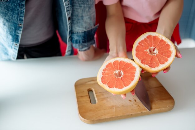 Joven y bella mujer están cortando pomelo en la cocina de casa