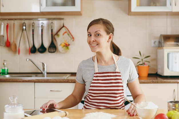 La joven y bella mujer feliz buscando una receta de pasteles en tableta en la cocina. Cocinar en casa. Prepara comida.