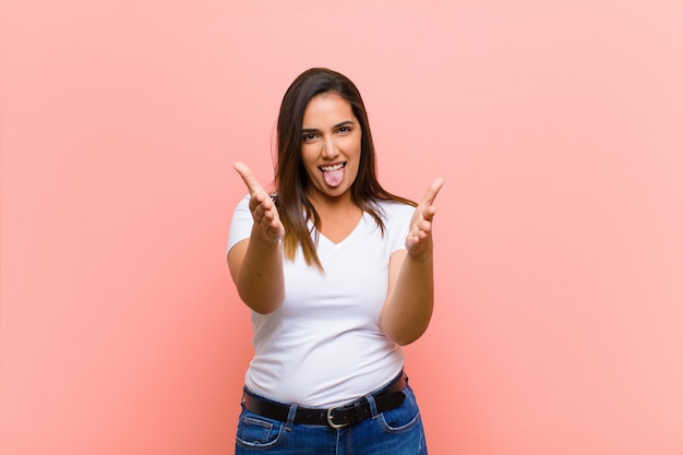 Joven y bella mujer hispana que se siente feliz, asombrada, afortunada y sorprendida, ¿como decir en serio? Increíble contra la pared rosa