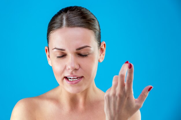 La joven y bella mujer de pelo castaño enojado y europeo con una piel sana y limpia, gritando y agitando los brazos sobre una pared azul. Concepto de emociones