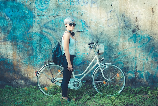joven y bella mujer de pelo corto azul hipster con auriculares y bicicleta