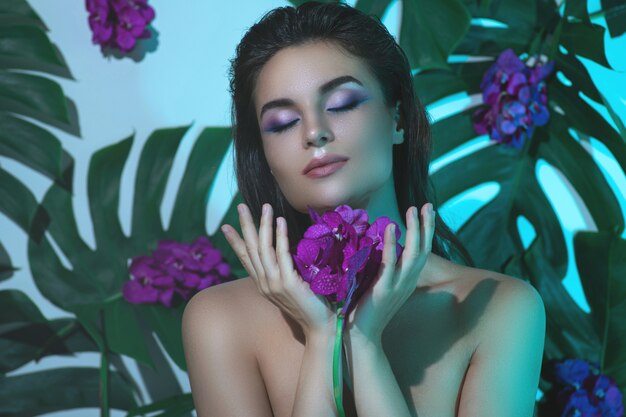 Joven y bella mujer con piel suave perfecta está sosteniendo flores de orquídeas