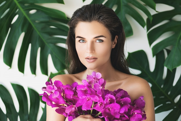 Joven y bella mujer con piel suave perfecta está sosteniendo flores de orquídeas