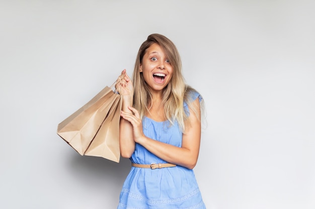 Una joven y bella mujer rubia sonriente caucásica con un vestido azul sostiene bolsas de papel ecológico en la mano