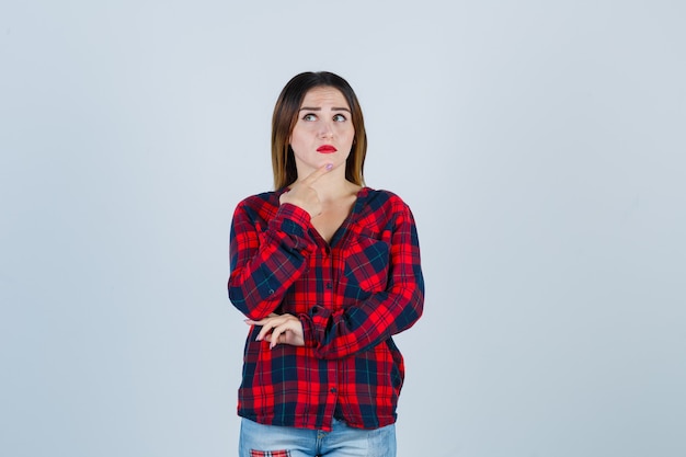 Foto joven y bella mujer sosteniendo el dedo en la barbilla en camisa casual y mirando de mal humor. vista frontal.