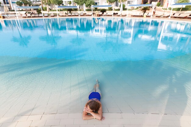 joven y bella mujer en traje de baño azul relajante en la piscina del hotel