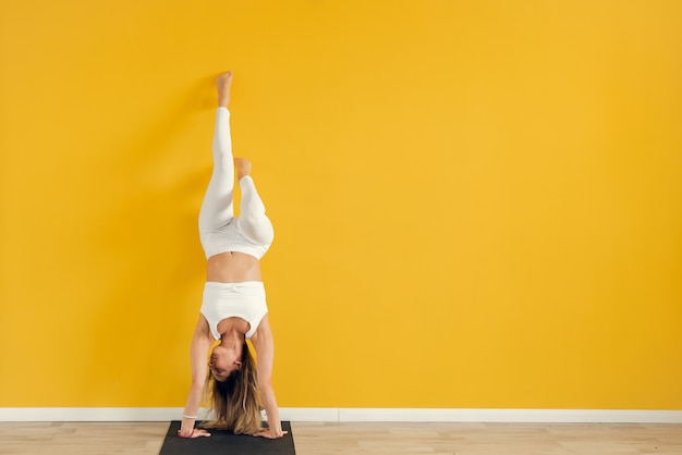 Una joven y bella mujer con uniforme deportivo realiza una difícil asana de  yoga, de pie