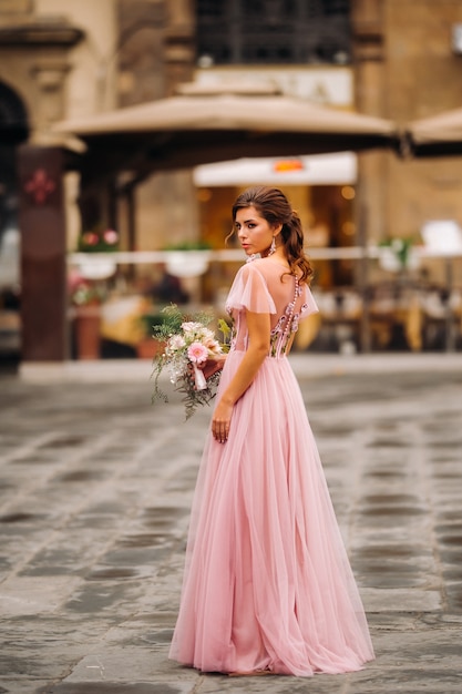 Una joven y bella novia se encuentra en el centro de la ciudad vieja de Florencia en Italia. Novia con un hermoso vestido rosa con un ramo de flores en Toscana, Italia.