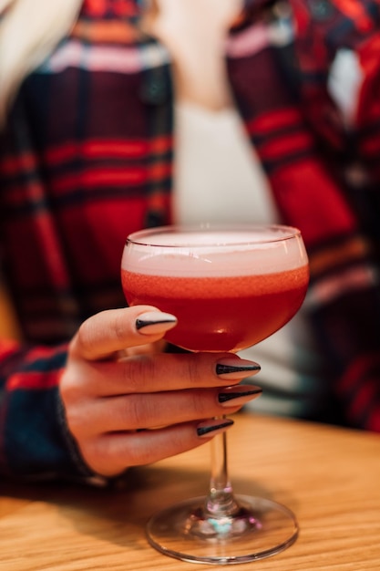 Una joven y bella rubia sostiene una copa con un cóctel en un restaurante.