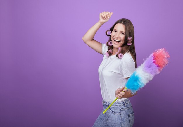 Una joven belleza en rulos canta canciones y bailes mientras limpia.