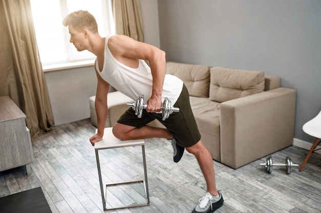 Joven bien construido hace deporte en apartamento