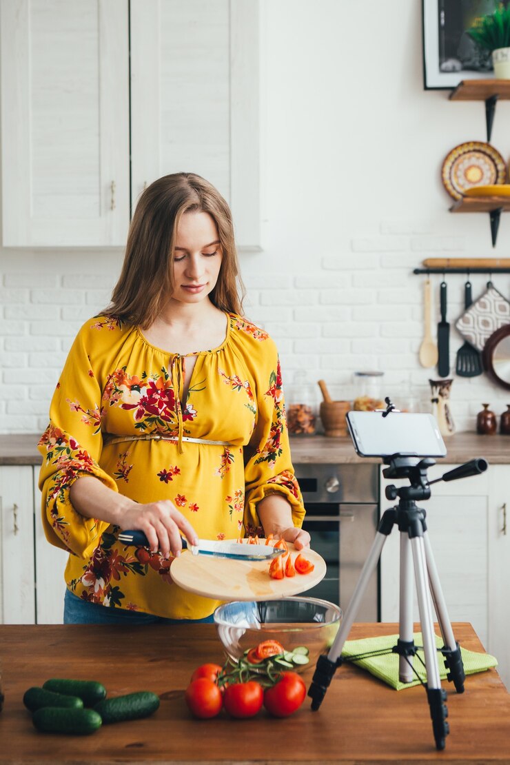Foto una joven blogger bastante embarazada graba un video de una receta de ensalada en la cámara de un teléfono inteligente