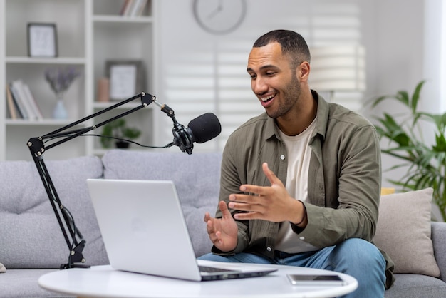 Joven blogger en casa en el sofá con una computadora portátil grabando un podcast en línea con un micrófono profesional