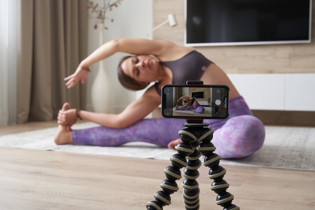 Joven blogger grabando videos deportivos en casa haciendo yoga en la sala de estar