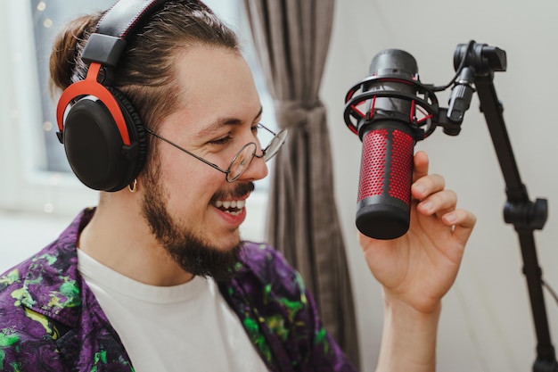 Foto joven blogger usando auriculares y micrófono de condensador durante la transmisión de podcast en línea