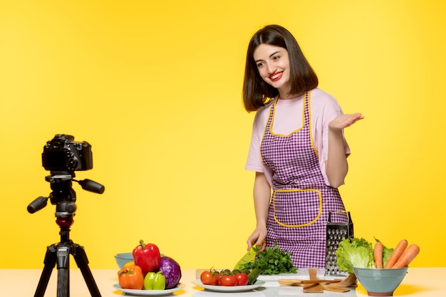 Joven bloguera de comida con delantal rosa grabando video para las redes sociales alegre cortando perejil