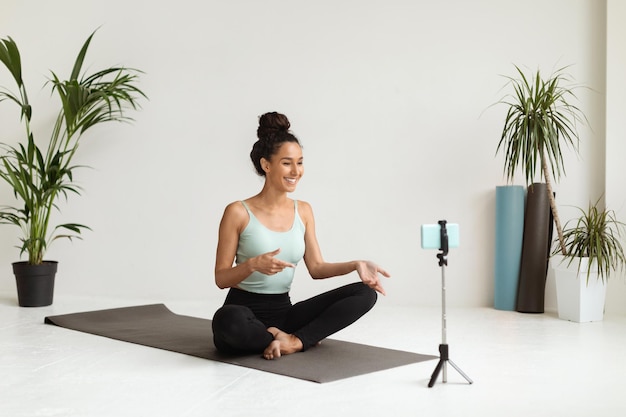 Joven bloguera de fitness capturando contenido de video con un teléfono inteligente en un estudio de yoga