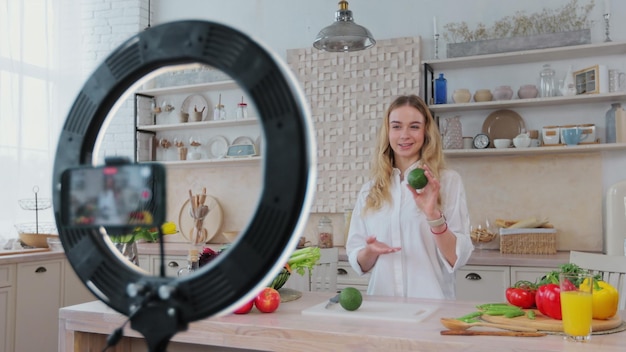 Joven bloguera o creadora de contenido preparando comida y grabando video en el teléfono Mujer mostrando cómo cocinar comida saludable y grabando blog con teléfono inteligente en la cocina