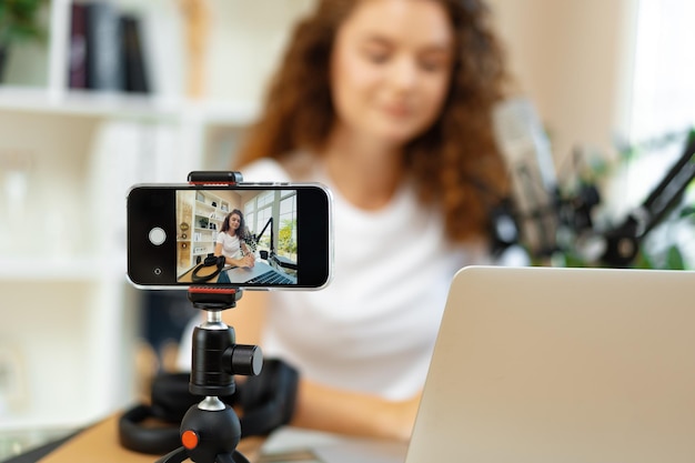 Foto una joven bloguera rizada grabando un video en la mesa de su casa.