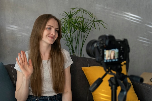 Una joven bloguera toma un video de sí misma en la cámara y agita su mano. Hermosa chica filmándose para vlogs