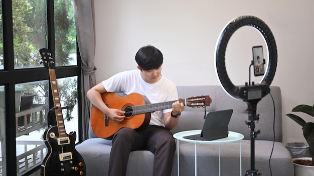 Joven bloguero de música transmitiendo video en vivo mientras toca la guitarra acústica en casa
