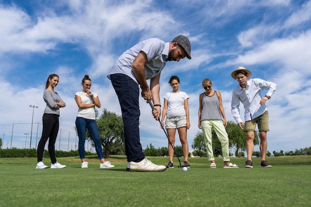 Joven con una boina jugando al golf con un palo de golf frente a un grupo de personas