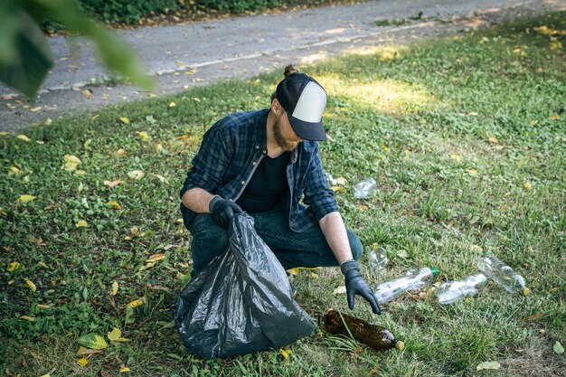 Foto un joven con una bolsa de basura en el bosque limpia botellas de plástico