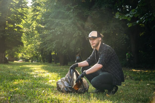 Un joven con una bolsa de basura en el bosque limpia botellas de plástico