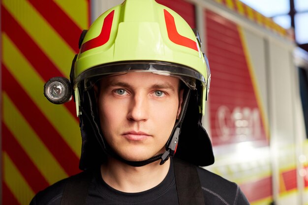 Un joven bombero uniformado parado frente a un camión de bomberos está listo para su despliegue