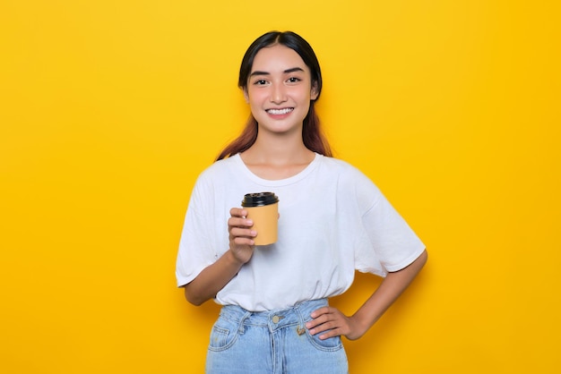 Una joven bonita y alegre con camiseta blanca sosteniendo una taza de café aislada de fondo amarillo