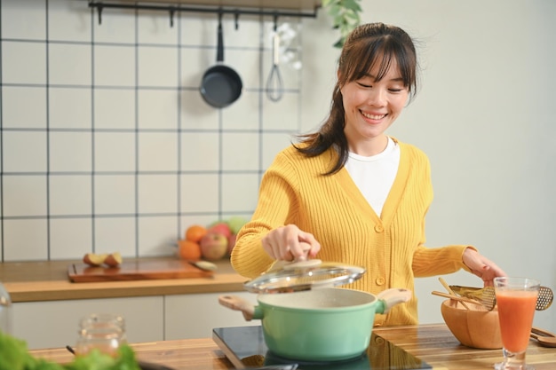 Una joven bonita en un cardigan amarillo claro está disfrutando de cocinar en la cocina de casa