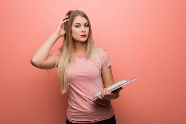 Joven bonita chica rusa preocupada y abrumada. Ella está sosteniendo libros.