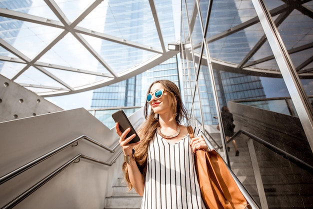 Joven y bonita empresaria de pie con el teléfono al aire libre en las escaleras cerca de las oficinas modernas en la ciudad de Bruselas