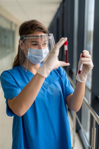 Joven bonita enfermera mirando una muestra de sangre para diagnóstico de coronavirus o COVID19